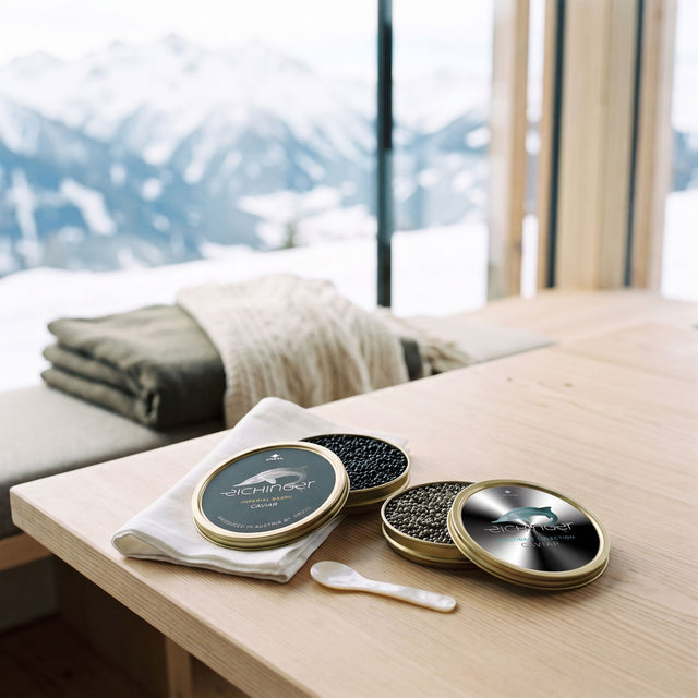 Boîtes ouvertes de caviar Eichinger Imperial Baerii et Platinum Selection sur une table en bois, sommets alpins enneigés en fond